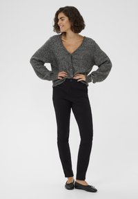 Hallikas, ülevõrreline kootud kardigan V-kaelusega ja nööbiga, koos mustade sobivate pükste ja mustade lamedate kingadega.