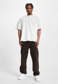 Camiseta blanca de gran tamaño, de mangas cortas, combinada con pantalones sueltos marrón oscuro y zapatillas blancas, diseño minimalista, estilo informal.