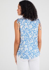 Top florale blu e bianco con spalline legate, scollatura rotonda e spacchi laterali sull'orlo; tessuto leggero e vestibilità comoda.