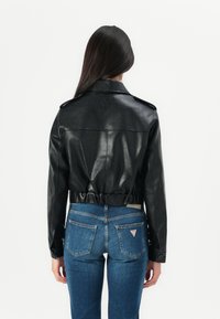 Svart lær cropped jakke med en glatt tekstur, skulderepauletter og innsnørt midje. Kombinert med blå denim jeans med et logo-patch.