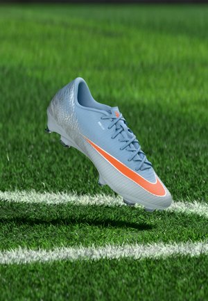 Chaussure de football bleu clair avec un swoosh orange flottant au-dessus d’une pelouse verte artificielle près d’une ligne blanche peinte.