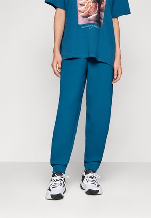 Teal joggebukser og en oversized teal T-skjorte med grafikktrykk, kombinert med svart-hvite sportsko. Myk, avslappet passform.