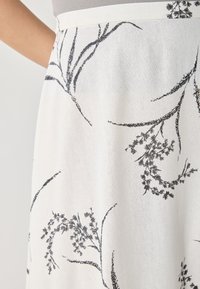 Vit tygkjol med svarta blommönster och lövverk, med en väldefinierad midja och slät textur.