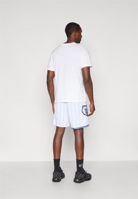 Tricou alb din bumbac, cu mâneci scurte; pantaloni scurți albi până la genunchi, cu dungi albastre și logo-ul unui urs; șosete negre și încălțăminte.