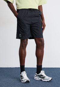 Shorts noirs légers avec une taille élastique, des poches latérales et un marquage discret en bas à gauche. Texture de tissu plate et respirante.