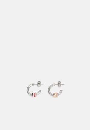Paire de petites boucles d’oreilles créoles en argent avec trois anneaux en or rose sur chacune, présentées sur un fond gris clair uni.