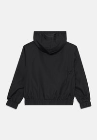 Jachetă neagră cu glugă, cu manșete și talie elastice. Material neted, rezistent la apă. Design minimalist; fără decorațiuni vizibile.