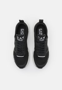 Zapatos deportivos negros con parte superior de malla y sintético, punta redonda y suela blanca en contraste. Cuenta con un diseño de cordones y un logo en la lengüeta.