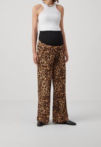 Vit ribbad halterneck-top, kombinerad med lösa bruna leopardmönstrade byxor. Byxorna har elastisk midja och sidofickor. Svarta slip-on skor.