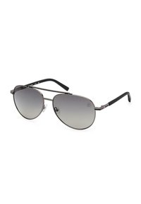 Gafas de sol tipo aviador con finos marcos de metal plateado, lentes grises degradados y puntas de las patillas negras, reposando sobre una superficie blanca.