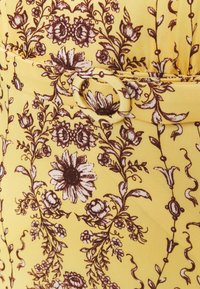 Gelber Stoff mit einem braunen Blumenmuster, das verschiedene Blüten und wirbelnde Ranken zeigt, akzentuiert durch einen passenden Gürtel mit einer runden Schnalle.