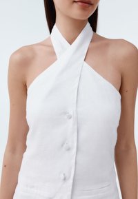 Fehér len anyagú pánt nélküli felső átkötős kialakítással, gombos záródással és ujjatlan kivitelben, amely sima textúrát és minimalista stílust hangsúlyoz.