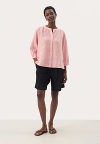 Red and white striped long-sleeve shirt with a round neckline and button front, paired with black shorts and brown flip-flops.