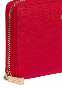 Red zippered wallet with a textured finish, gold hardware, and logo tag. Features a sleek rectangular shape and subtle diagonal pattern.