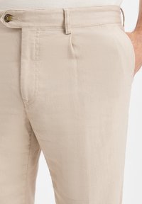 Pantaloni in lino beige con frontale piatto, tasche laterali, chiusura con bottone e una texture liscia. Dettagli di cucitura visibili lungo le cuciture.