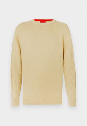 Krämfärgad tröja med en strukturerad design, rund halsringning och ribbade manschetter. Har ett subtilt logomönster över hela plagget.