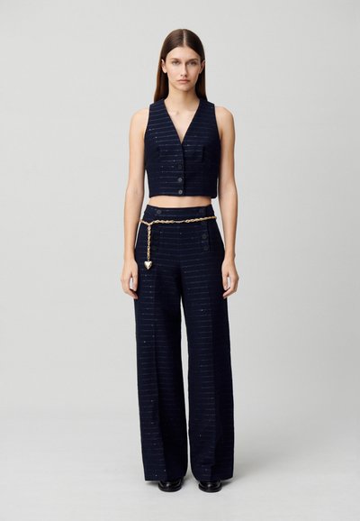 Ensemble deux pièces marine composé d'un top cropped sans manches avec des boutons et un pantalon large, accentué d'une ceinture en chaîne dorée et d'un motif rayé.