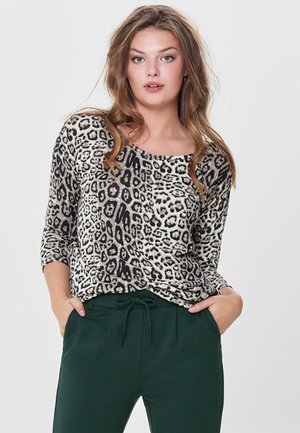 Sweater med leopardprint, rund halsudskæring og trekvartærmer; lavet af blødt stof. Båret med grønne joggerbukser.