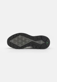 Black rubber sole with a textured tread pattern, featuring raised cross shapes and a green accent near the heel for traction and durability.