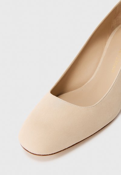 Pantof beige din suede, cu vârful ascuțit, decolteu în față, căptușeală interioară netedă și talpă plată de culoare tan. Fără ornamente sau modele vizibile.