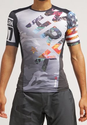 T-shirt de sport à manches courtes gris avec motif camouflage. Présente des éléments graphiques colorés et un design de drapeau américain sur la manche.