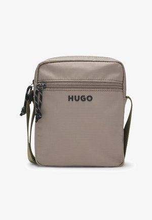 Kompaktowa beżowa torba na ramię z przednią kieszenią na zamek, czarnymi suwaczkami, oliwkowo-zielonym regulowanym paskiem oraz logo "HUGO" z przodu.