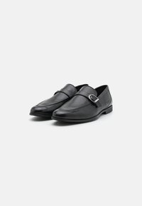 Mustad mustad nahast loafers, ümarate varvastega, õmmeldud detailide ja läikiva pandla kaunistusega; sile pind ja tasane tald.