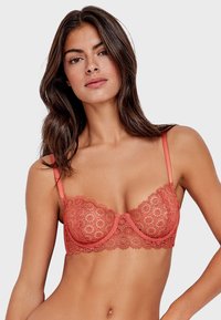 Soutien-gorge arancione in pizzo con motivo floreale, supporto con ferretto e spalline regolabili. Presenta bordi ondulati e un design trasparente.