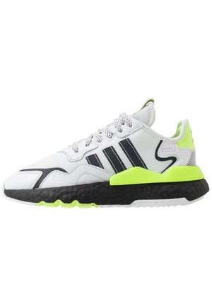 Baskets de sport blanches avec des bandes noires, des accents verts fluo, une semelle noire texturée et des lacets blancs à motifs, vues de profil.