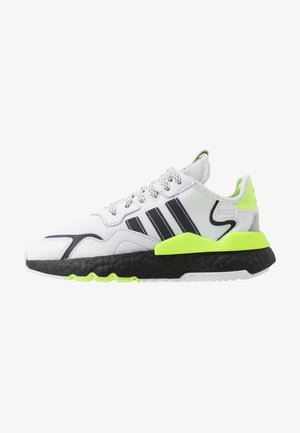 Biały sportowy sneaker z czarnymi paskami, neonowo zielonymi akcentami, czarną teksturowaną podeszwą i białymi wzorzystymi sznurowadłami, widziany z boku.