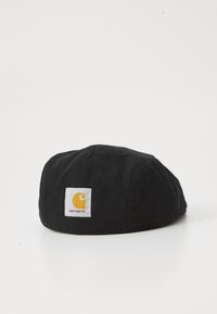 Cappello nero realizzato in tessuto resistente, con un'etichetta quadrata bianca e un emblema giallo. Forma arrotondata con dettagli cuciti.