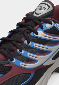 Κοντινό πλάνο μαύρου, μπλε και μαρόν αθλητικού παπουτσιού με μαύρα κορδόνια, ύφασμα από δίχτυ, πλαστικές επενδύσεις και γλώσσα με λογότυπο.