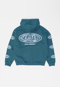 Sweat à capuche bleu sarcelle avec logo ovale blanc déformé et texte "STWD COMMUNITY" au dos, accompagné de logos assortis plus petits sur les manches.