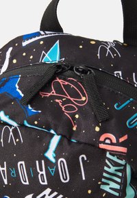Le sac à dos en tissu noir présente des graphismes et des motifs colorés, un compartiment zippé et des zips texturés noirs avec des languettes en nylon.