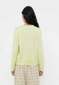 Πράσινο ανοιχτό πλεκτό πουλόβερ με στρογγυλή λαιμόκοψη, μακρύ μανίκι και ριμπ τελείωμα. Συνδυάζεται με καρό μπεζ παντελόνι.