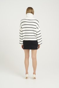 Hvit og svart stripete turtleneck-genser, ribbet tekstur, cropped design. Kombinert med et svart denim miniskjørt og lyse hæler.