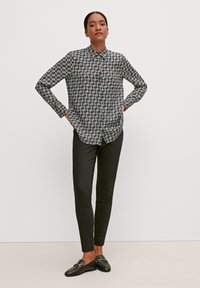 Black-and-white patterned button-up shirt with long sleeves, paired with black skinny pants and black loafers. Smooth fabric texture.