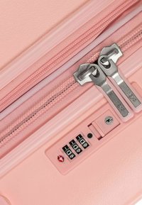 Valigia rigida rosa chiaro con doppie cerniere metallizzate, lucchetto a combinazione integrato e texture interna a contrasto.