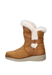 Tan suède enkellaarzen met witte bontvoering aan de bovenkant, decoratieve zilveren studs, stevige zool en een banddetail aan de zijkant.