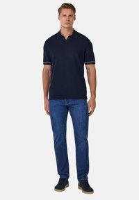 Polo de color navy con mangas cortas, con ribete blanco en los puños, combinado con jeans azules y zapatos negros. Material de mezcla de algodón.