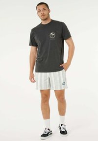 Maglietta grigia in cotone con logo a palma, abbinata a pantaloncini a righe bianchi e grigi. Include scarpe da ginnastica nere e calzini alla caviglia bianchi.