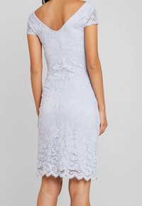 Světle modré krajkové šaty se formovaným střihem, krátkými rukávy a zvlněným lemem. Obsahují květinové vzory a detailem ve tvaru V na zádech.