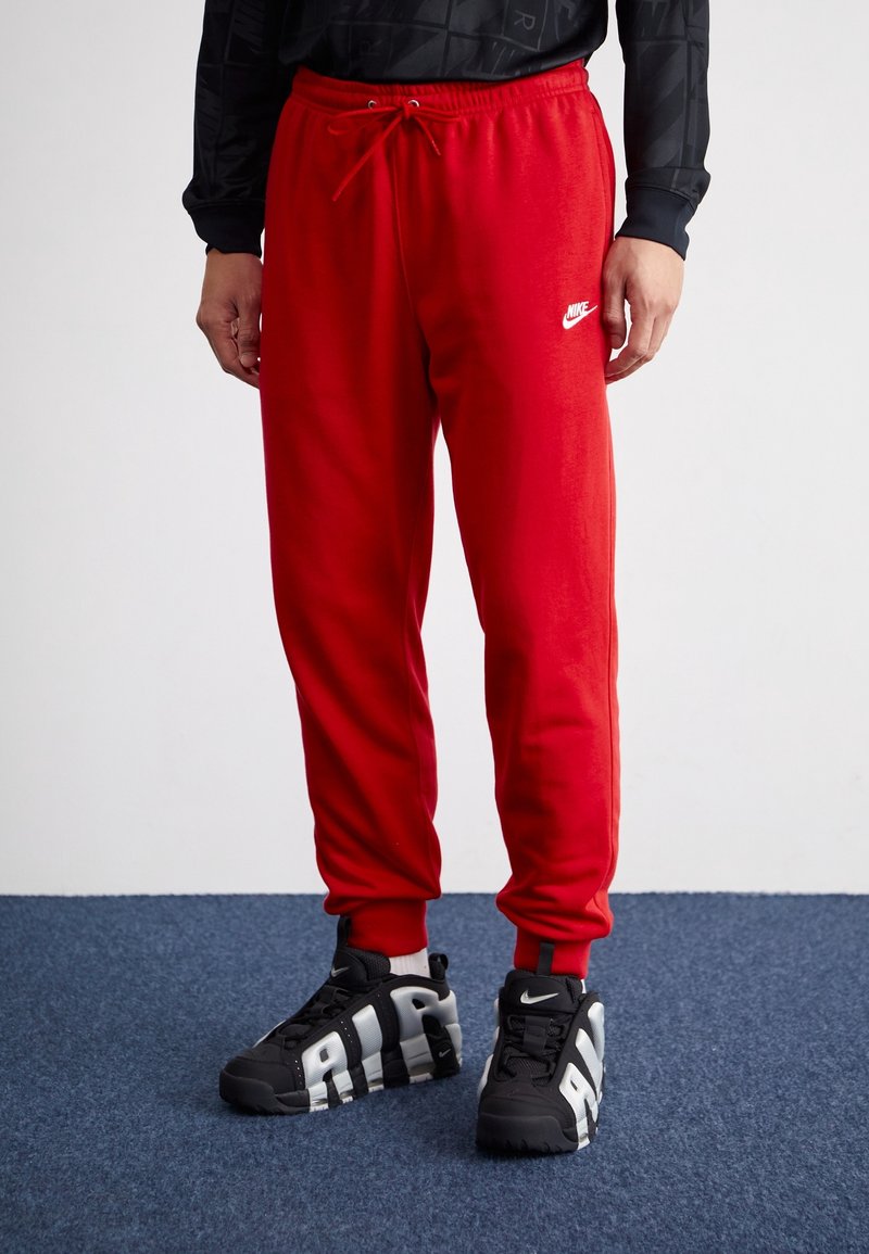 Pantalons de survêtement rouges avec taille élastique et cordon, arborant un logo Nike blanc. Associés à des baskets noires avec des accents gris audacieux.