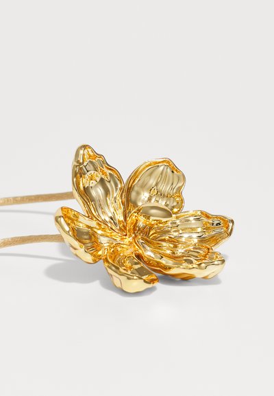Accessorio per capelli floreale in oro, caratterizzato da un design dettagliato dei petali, una finitura metallica liscia e un elastico marrone chiaro per una tenuta sicura.