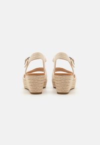Sandali con zeppa beige caratterizzati da un design con cinturino intrecciato, una fibbia regolabile e un tacco in corda testurizzato. Soletta liscia con minimi dettagli.