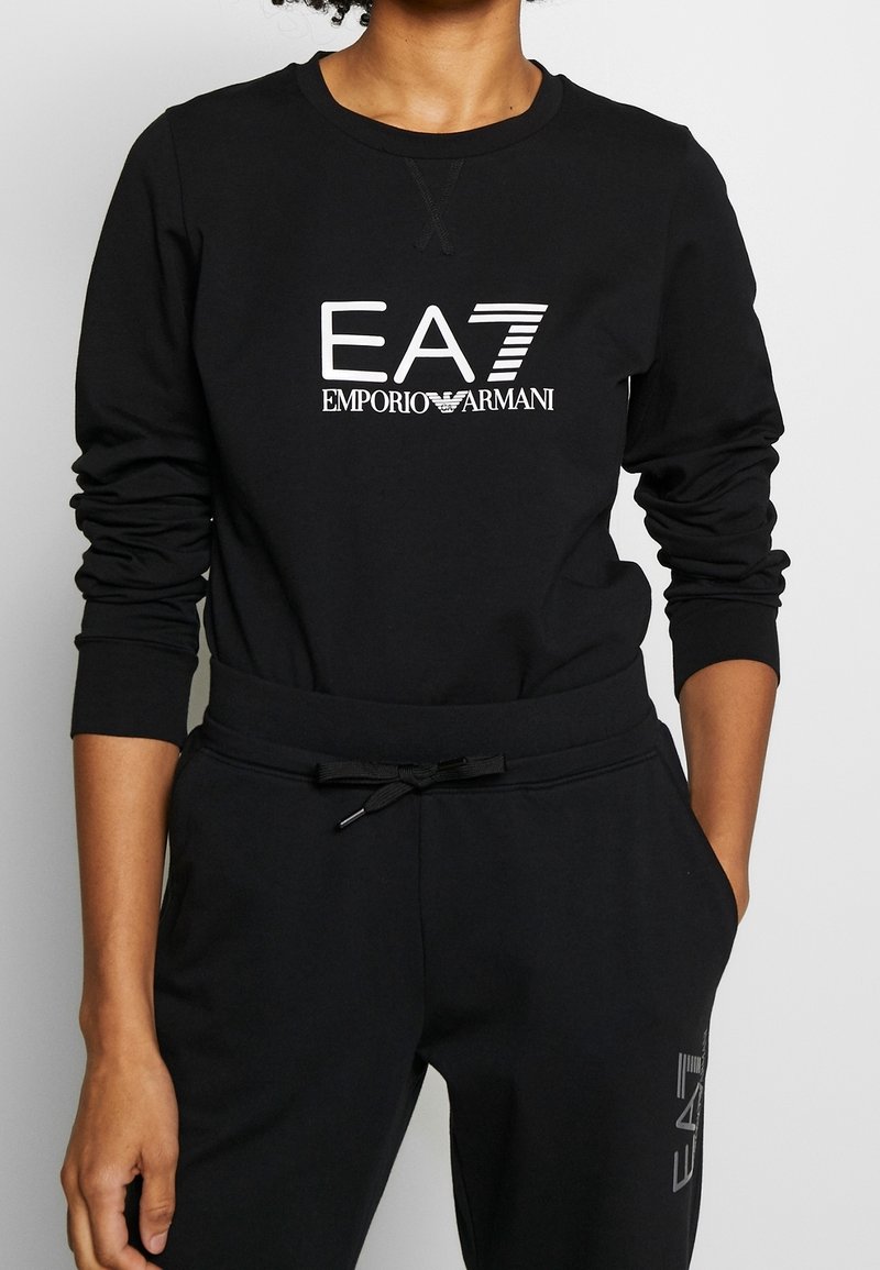 Svart sweatshirt och byxor med "EA7 EMPORIO ARMANI"-logotyp i vitt, mjukt tyg, avslappnad passform, ribbade ärmslut och dragsko i midjan.