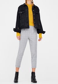 Veste en denim noir, pull en tricot jaune moutarde, pantalon à carreaux gris et bottines noires. La veste a une coupe décontractée et des détails de boutons.