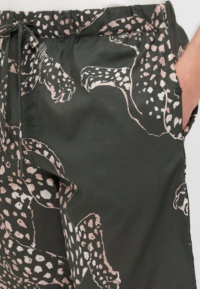 Pantalon vert foncé avec un grand motif à pois rose pâle. Dispose d'une taille élastique, d'un cordon de serrage et de poches latérales.