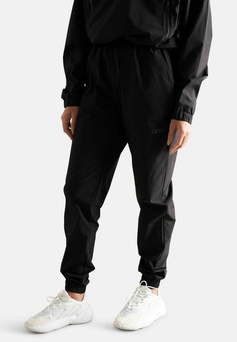 Joggers neri con cintura elastica e caviglie strette, realizzati in tessuto leggero. Presentano un sottile dettaglio del logo sul lato e un design elegante.