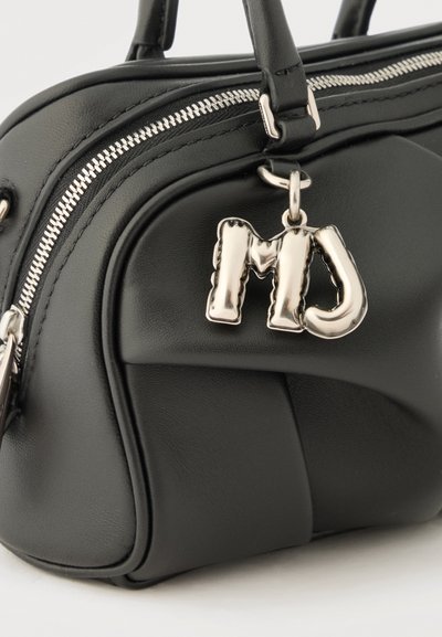 Μαύρη δερμάτινη τσάντα χειρός με ασημί φερμουάρ και μεταλλικό διακοσμητικό σε σχήμα γράμματα "MJ" που είναι προσαρτημένο στη λαβή.
